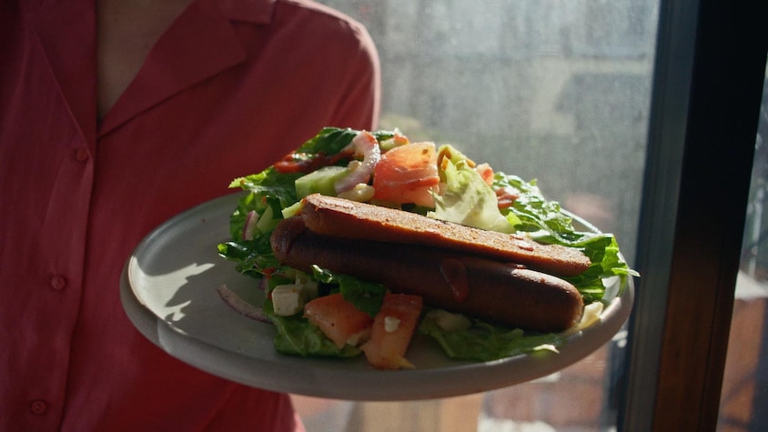 Une salade de légumes avec 2 saucisses sur une assiette.