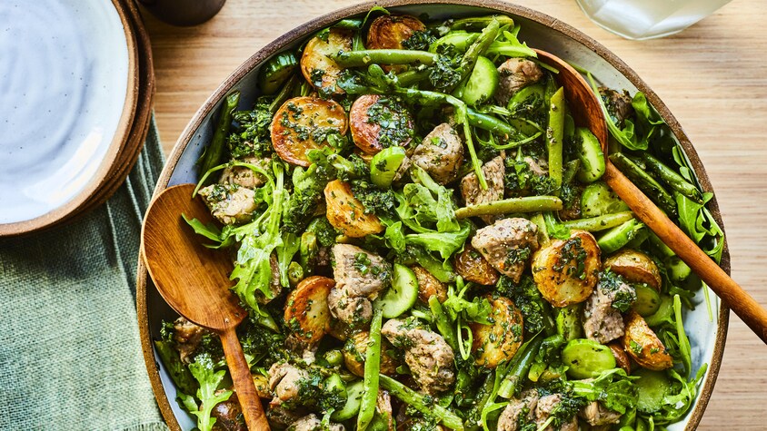 Un grand bol rempli de salade d'agneau au chimichurri avec des ustensiles de service dedans. 