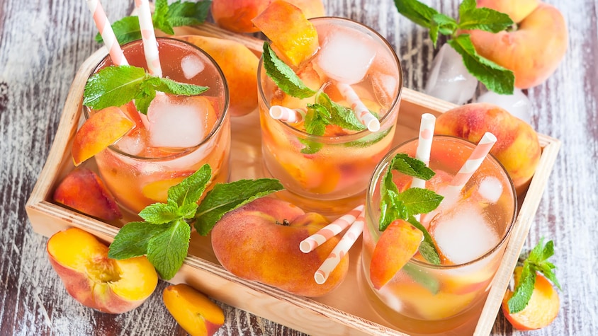 Trois verres de sangria blanche avec des pêches et de la menthe.