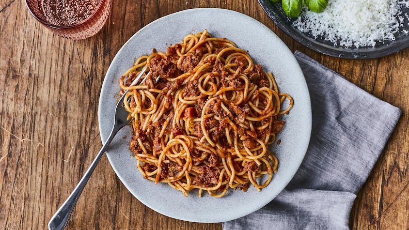 Une assiette de spaghetti avec un verre d’eau pétillante et un bol de parmesan. 