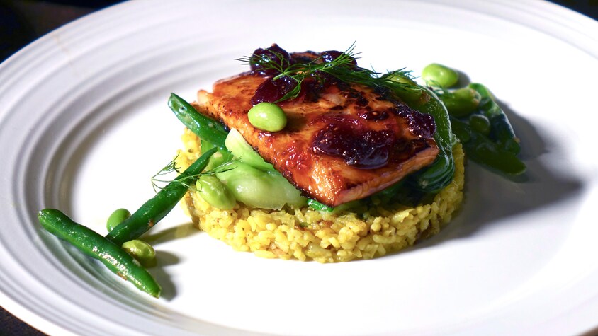 Un morceau de saumon laqué déposé sur du riz pilaf persan et des légumes verts.