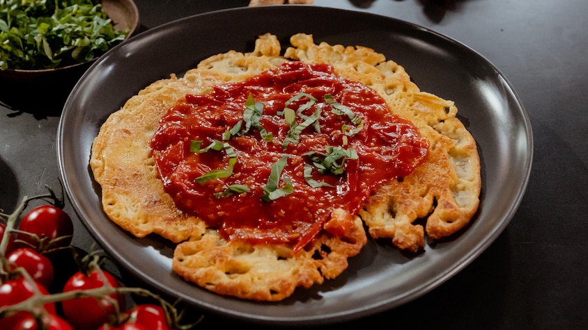 Une crêpe socca recouverte d'une compote de tomates cerises dans une assiette.