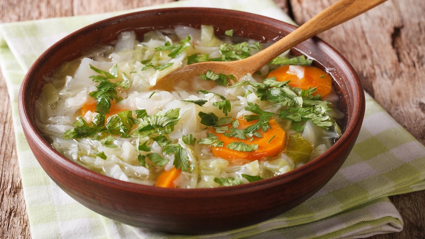 Un bol rempli de soupe au chou, carotte et herbe fraîche.