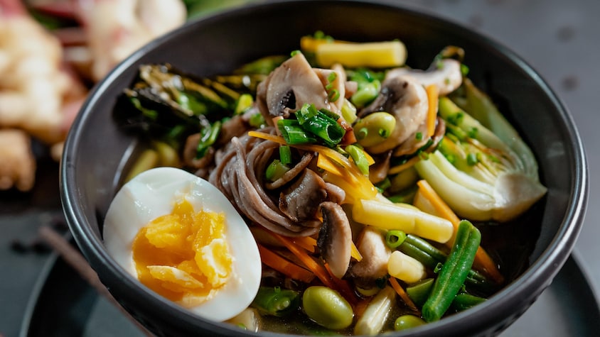 Un bol rempli de soupe de nouilles soba, de légumes, avec un œuf cuit.