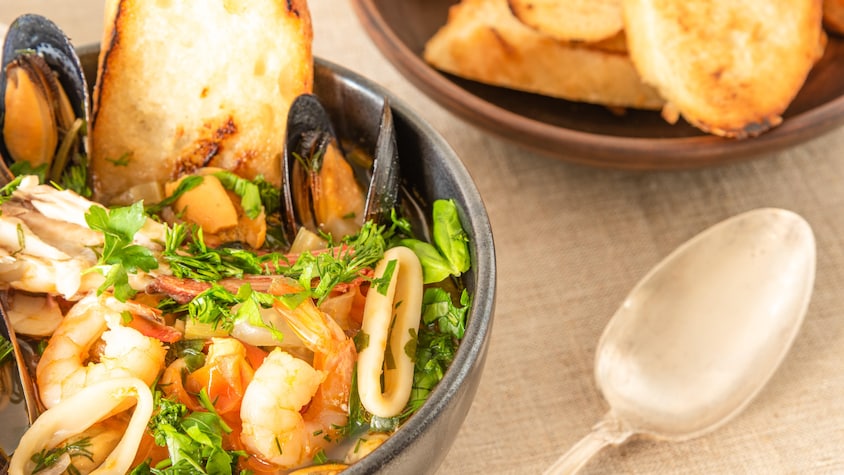Un bol de soupe avec calmars, crevettes, moules et pain. 