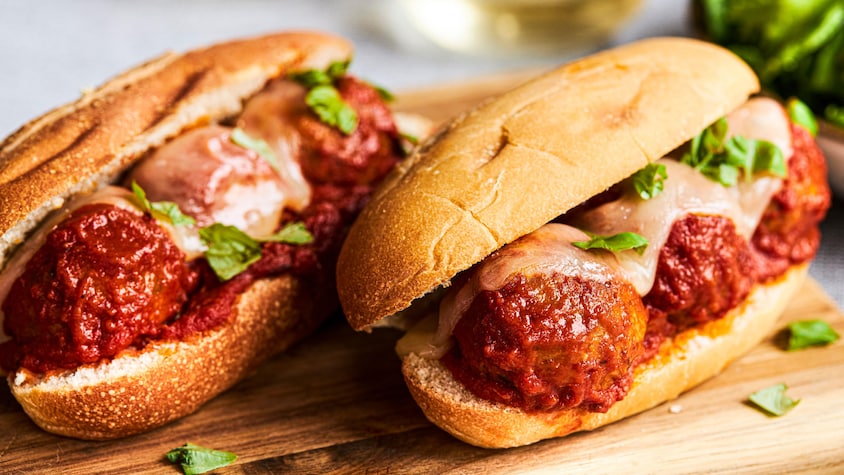 Deux sous-marins de boulettes végétariennes garnis de fromage fondu et posés sur une planche de bois.