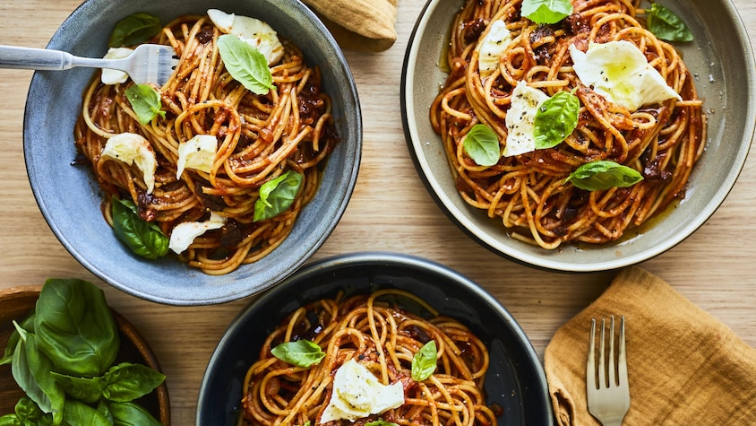 Bols de spaghetti aux tomates et au pesto posés sur une table en bois.