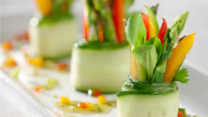Une assiette avec trois roulés de concombre farcis d'asperges, de laitue, de poivrons et de fines herbes.