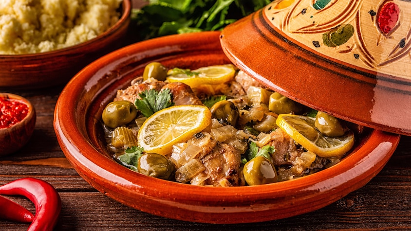 Un plat tajine remplit de morceaux de poulet, d'olives et de tranches de citron confit.