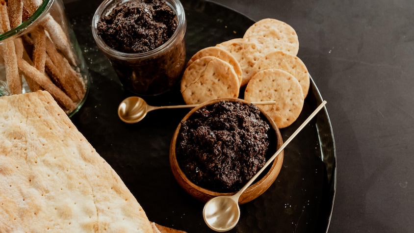 Deux bols remplis de tapenade aux olives noires avec de petits biscuits salés.