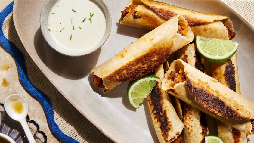 Des taquitos aux haricots pinto BBQ et un bol de sauce dans une assiette de service.