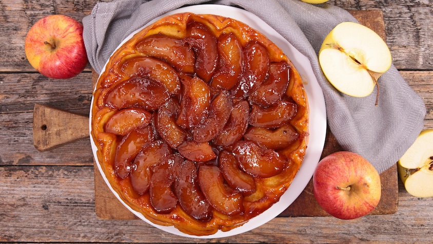 Une tarte Tatin entourée de quelques pommes.