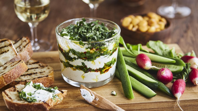 Tartinade étagée de fromage de chèvre aux herbes et à l’huile d’olive dans un plat en verre.