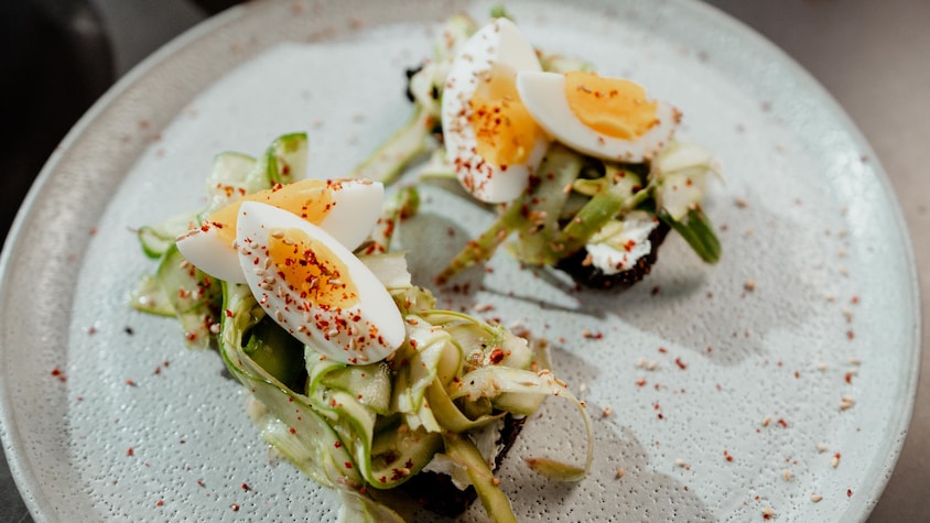 Deux tartines aux asperges, aux concombres et aux œufs dans une assiette blanche.