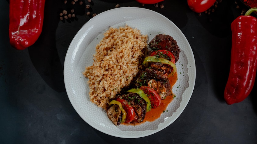 Une assiette de tian de kebabs, de légumes et de pilaf.