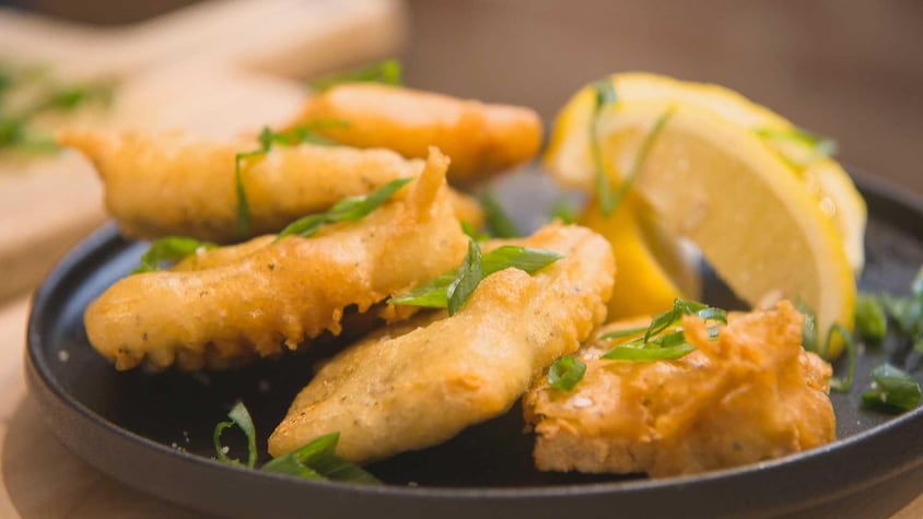 Des morceaux de tofu panés accompagnés de deux quartiers de citrons dans une assiette.