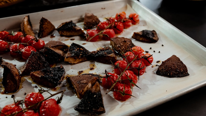 Des tomates cerises et des morceaux de champignons portobellos sur une plaque de cuisson sortant du four.