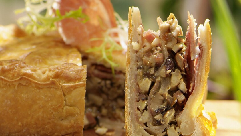 Tourte farcie de champignons bolets et de jambon sur une planche de bois.