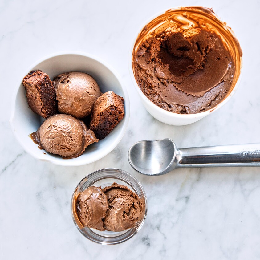 Un bol de crème glacée au chocolat avec un bol rempli, un pot de verre et une cuillère pour la servir.