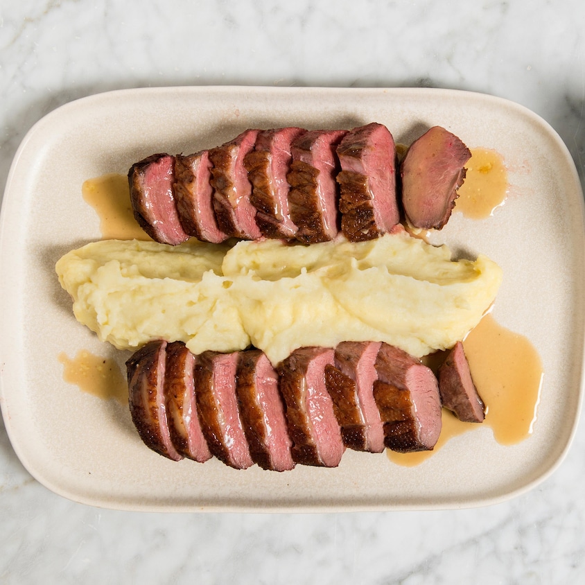 Dans une assiette, du magret de canard en tranches avec de la purée de pommes de terre. À la droite de l'assiette se trouve un saucier rempli de sauce aux épices et whisky.