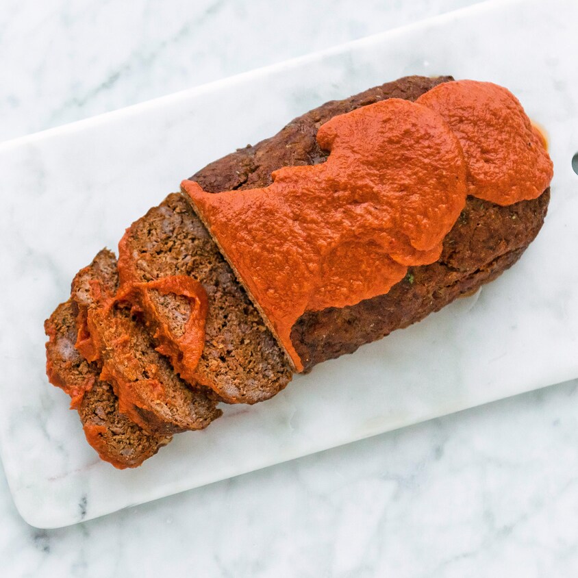 Sur une planche à découper, il y a un pain de viande avec de la sauce tomate sur le dessus.