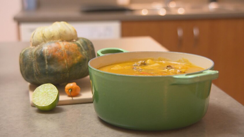 Un chaudron de soupe joumou et une courge giraumon sur un comptoir de cuisine.