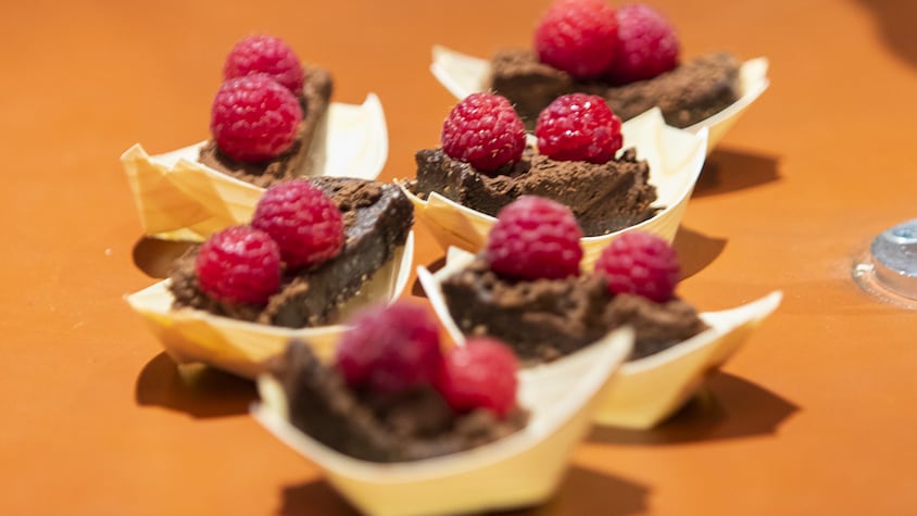 Des brownies véganes, décorés de framboises et servis dans de petites barquettes de carton.