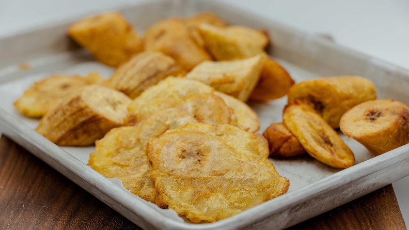 Des morceaux de bananes plantains frites jonchent une plaque à cuisson.