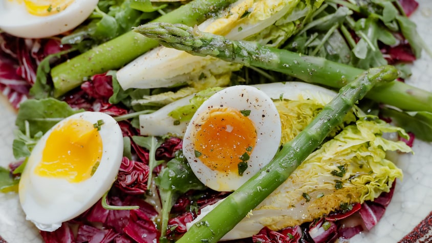 Une salade repas avec des œufs, des asperges et un mélange de laitues.