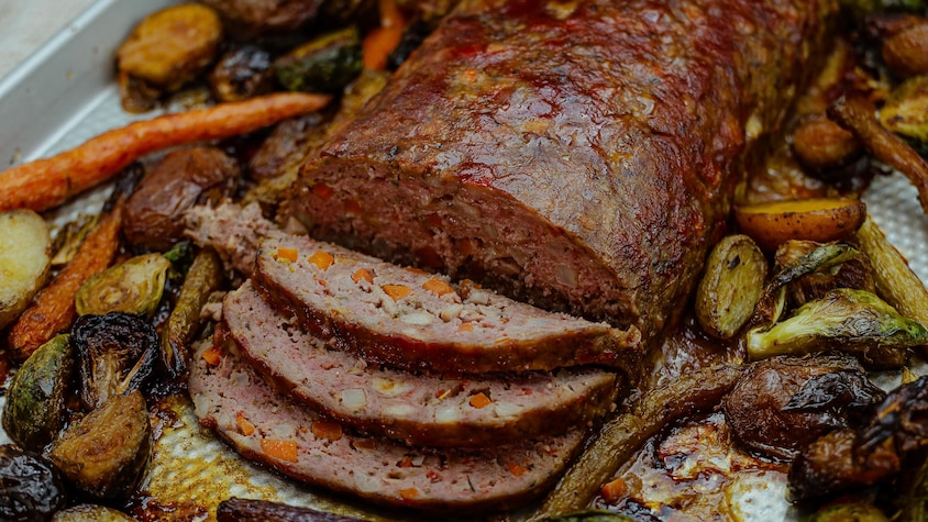 Un pain de viande cuit sur une plaque, entouré de légumes rôtis.