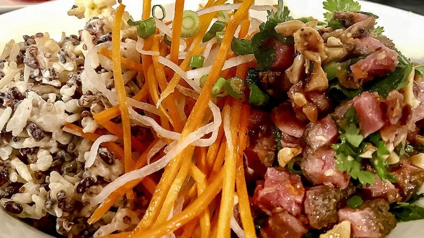 Un bol est composé de riz, de viande, de carottes râpées et d'herbes fraîches.