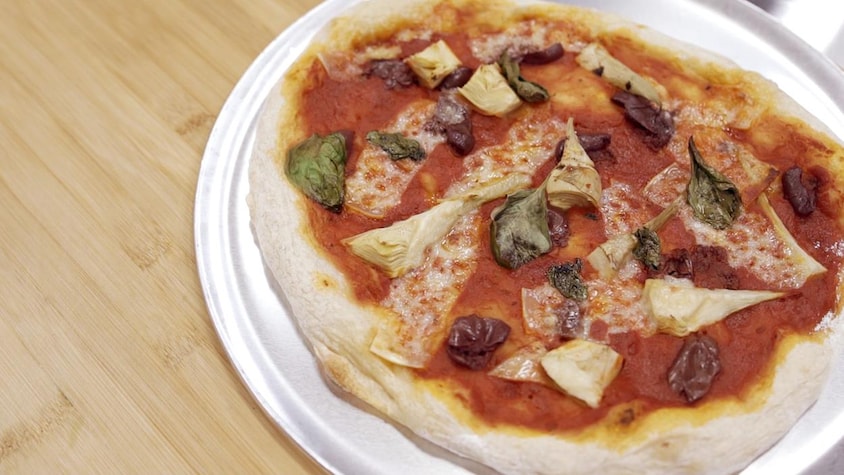 Une grande pizza tomates, olives, artichauts et fromage présentée sur une plaque à pizza.
