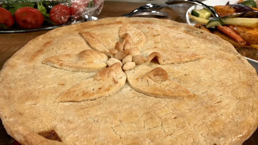 Une tourtière bien dorée et décorée de feuilles en pâte au centre.