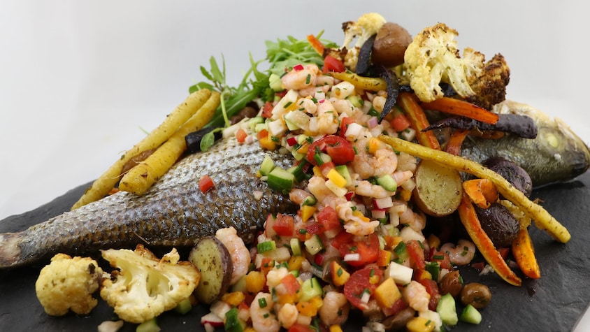Un poisson entier recouvert de crevettes et de légumes.