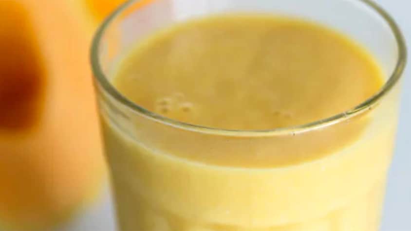 Un verre de smoothie orange à côté d'un demi melon.