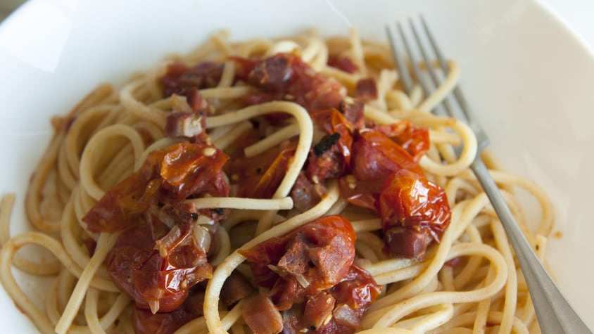 Un bol de spaghettis avec des tomates cuites au four et de la chair de saucisses.