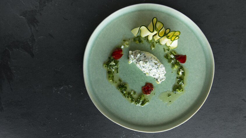 Une assiette avec du fromage crémeux, de l'huile, du pesto et des tranches de zucchinis.