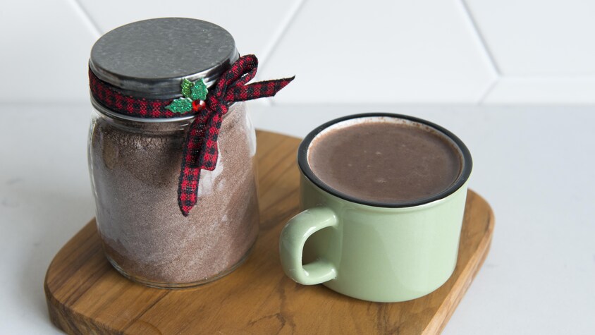 Une tasse de chocolat chaud est à côté d'un pot en verre rempli de poudre de chocolat.