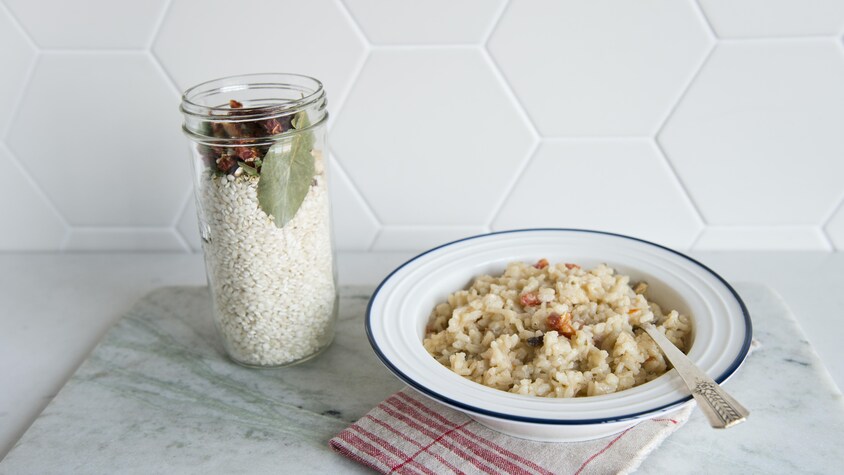Un pot en verre avec les ingrédients du risotto est à côté d'un plat de risotto.