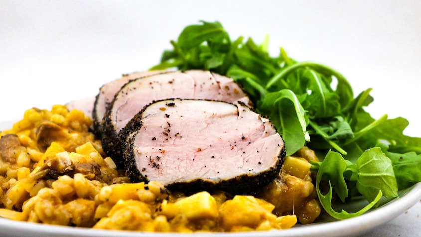 Le risotto est servi avec des tranches de porc et une salade de roquette.