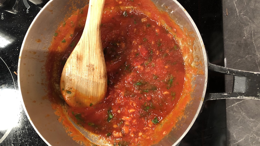 Un chaudron sur une plaque de cuisson contient une sauce tomate et une cuillère de bois