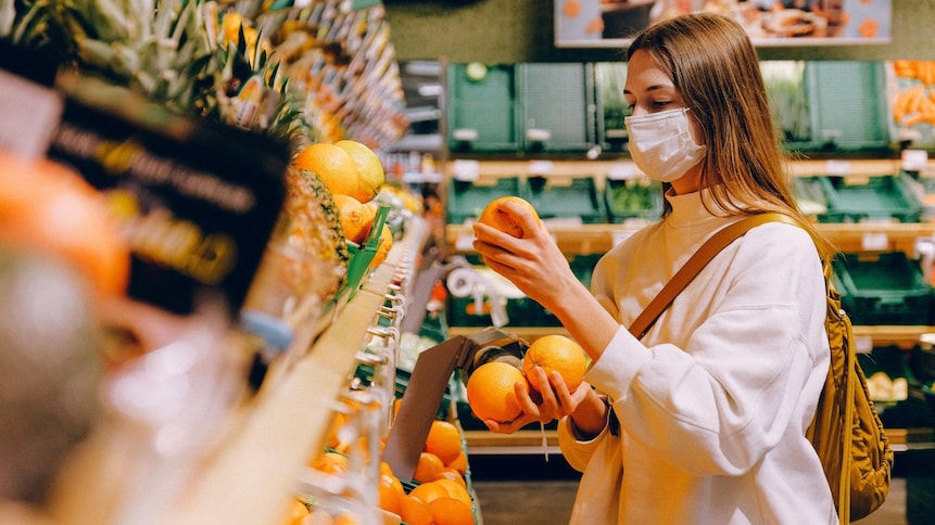 Une jeune femme masquée choisit des oranges au marché.