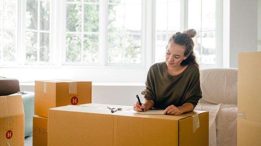 Une jeune femme écrit sur des boîtes de déménagement.