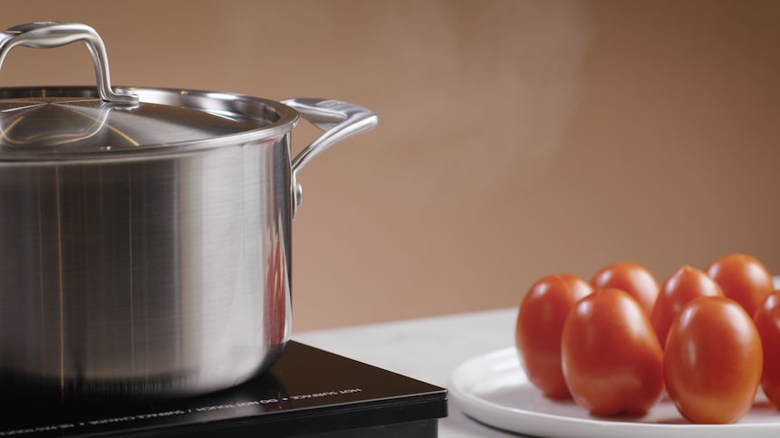 Un chaudron est déposé sur une plaque de cuisson. À sa droite, des tomates sont déposées dans une assiette.