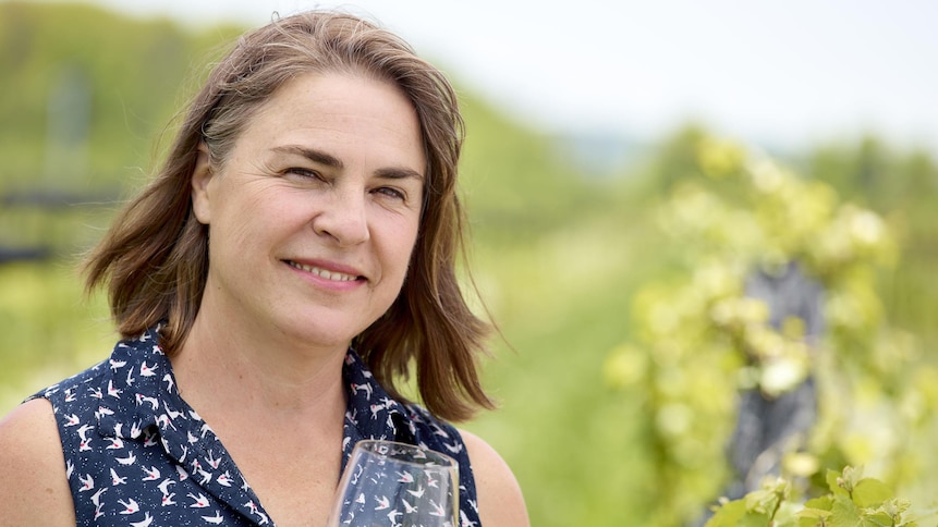 La vigneronne Ann Sperling dans son vignoble, un verre de vin blanc à la main.