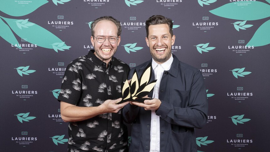 Les deux hommes sourient en tenant un trophée.