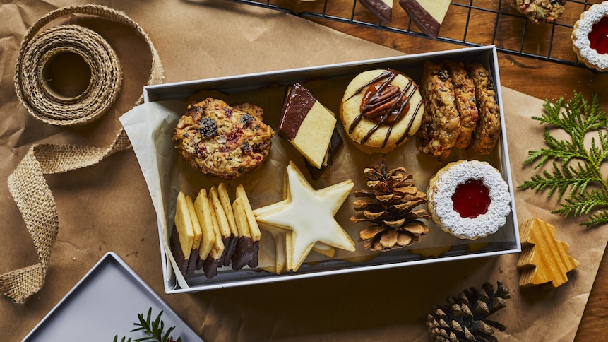 Une variété de biscuits de Noël disposés dans une boîte blanche entourée de rubans et de décorations de Noël. 