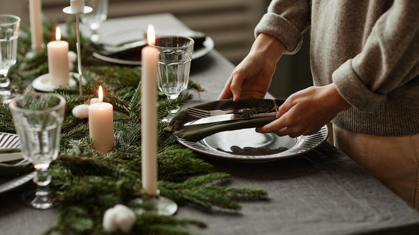 Une personne dépose ustensiles et vaisselles sur une table décorée pour Noël.