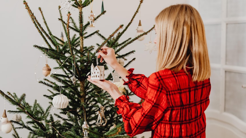 Une femme accroche une décoration de Noël dans un sapin.