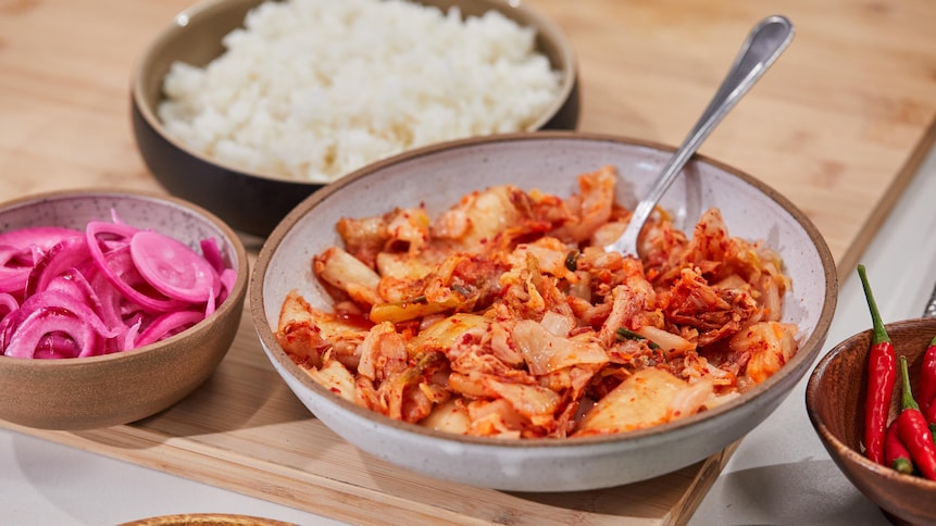Un bol de kimchi, de riz, de piments forts, d'oignons marinés, de concombres et d'oignons verts sur un comptoir.